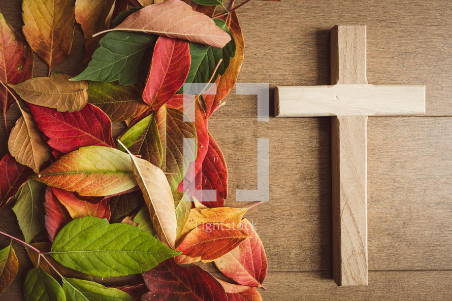 Autumn leaves and wood cross on a light wood background