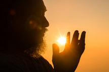 Silhouette of a man with a beard praying at sunset