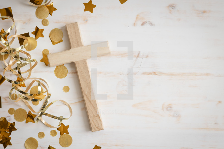 Gold confetti and streamers with a small wood cross on a white background with copy space
