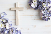 Wood cross and frame of purple silk flowers on a white wood background