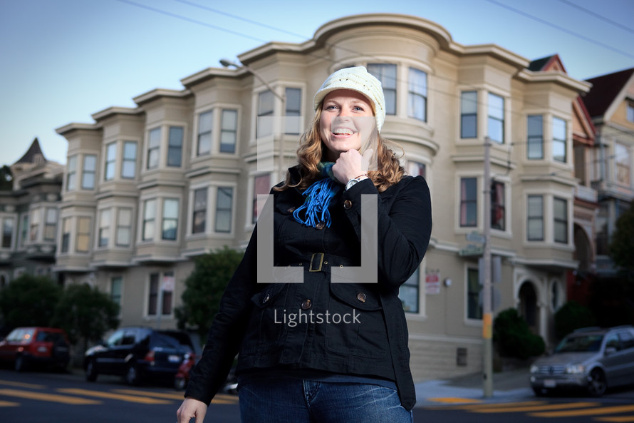 woman in a toboggan and scarf standing in front of apartments 