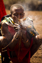 man blowing on embers in a village 