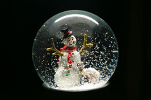 a snowman in a snow globe against a black background 