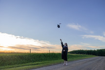 female graduate in cap and gown near a rural field 