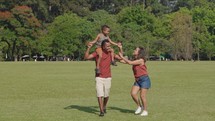 Cute latino boy and his parents are playing in the park. Family have fun during a weekend in nature.
