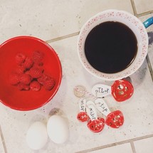 Ingredients on tile: coffee, raspberries, eggs, and measuring spoons.