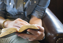 woman sitting in a leather chair reading a Bible 