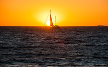 Silhouette of a sailboat in the ocean water at sunset.