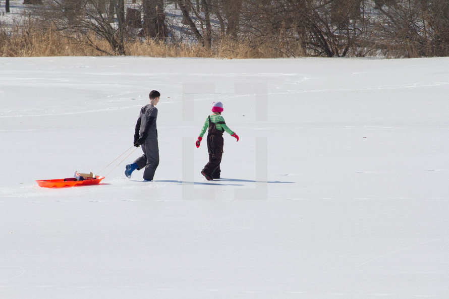 children dragging a sled in snow 