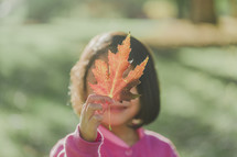 a young girl holding up a fall leaf 