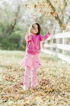 a young girl throwing fall leaves 