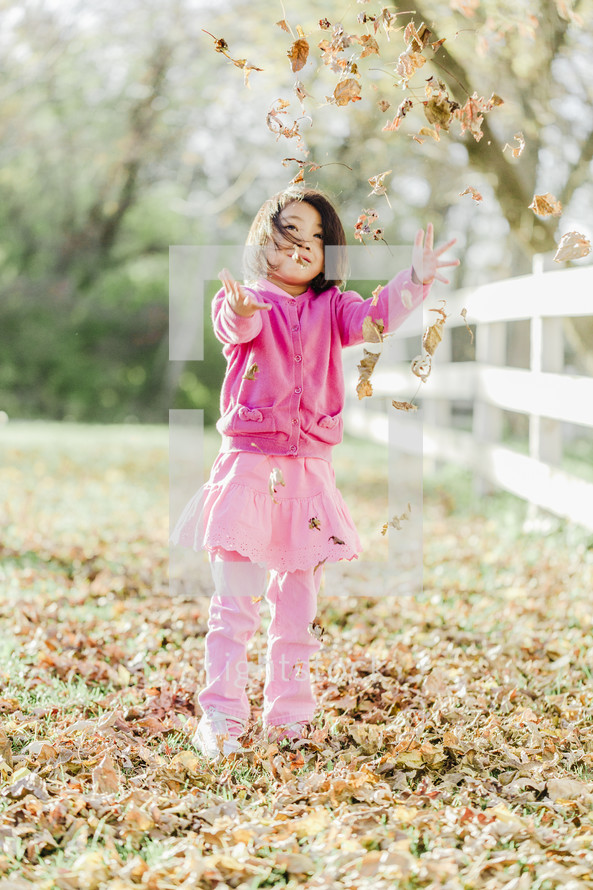 a young girl throwing fall leaves 