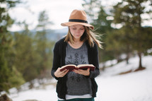 a young woman reading a Bible outdoors in snow 