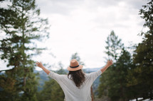 a woman in a hat with open arms on a mountaintop 