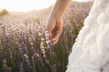 bride walking through a field touching purple wildflowers