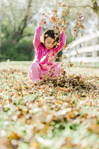a young girl throwing through fall leaves 