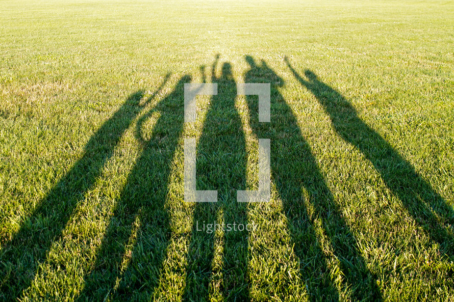 shadows of people with raised hands in the grass 