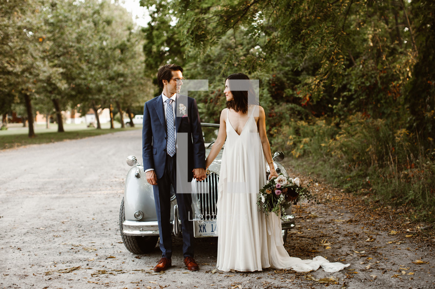 bride and groom standing in front of an old car