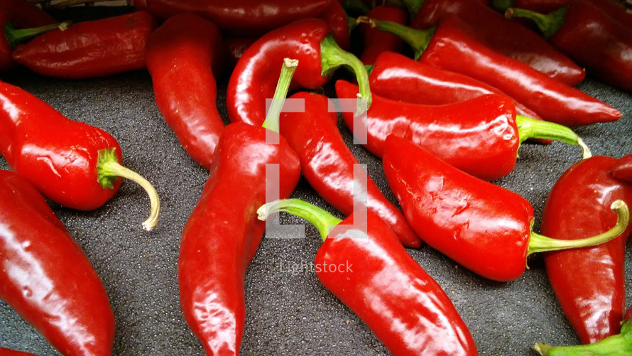 A group of red shiny peppers draw the eye and reflect light in the produce stand to attract the eye and show it is good to eat. Spicy, hot food ideal for the summer time or to add to barbecues, tacos or salads.