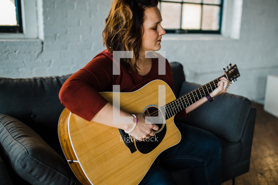 a woman sitting on a couch playing a guitar 