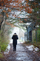 a woman walking on a muddy dirt road with melting snow