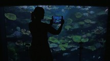 Young woman at the oceanarium take pictures of fish