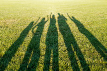 shadows of people with raised hands in the grass 