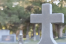 blurred photo of a cemetery with emphasis on large cross monument off-center