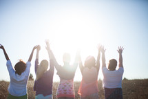 women with raised hands outdoors in a field 