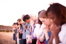 group of people with heads bowed and praying hands outdoors