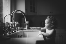 toddler playing in water at the kitchen sink 