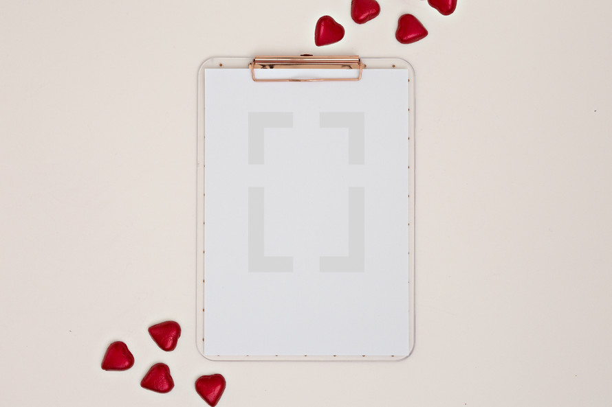 red heart shaped chocolates and white paper on a clipboard 