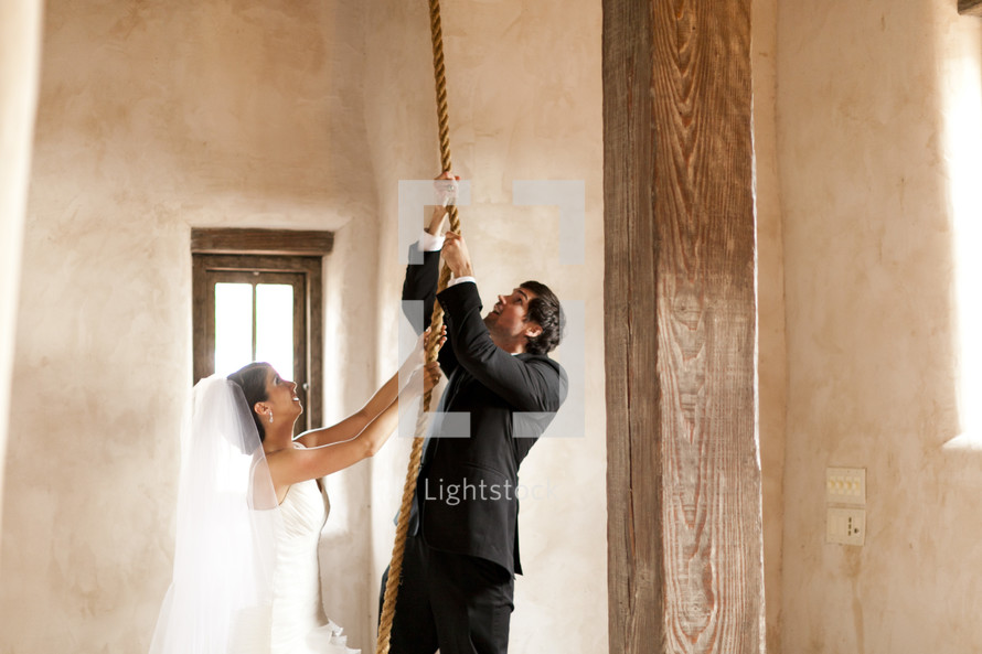 A bride and groom pull on a rope in order to ring the bell tower