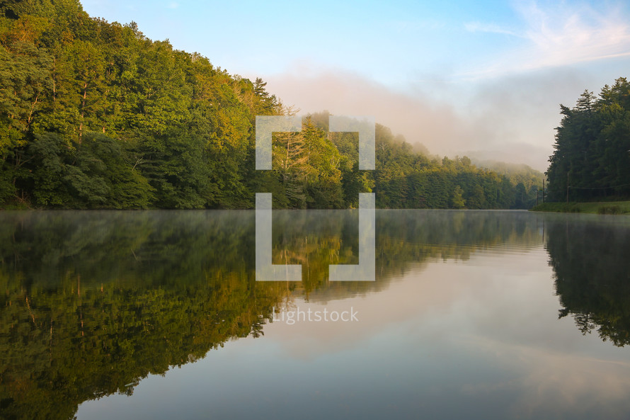 Evergreen trees and misty sky reflecting on still lake 