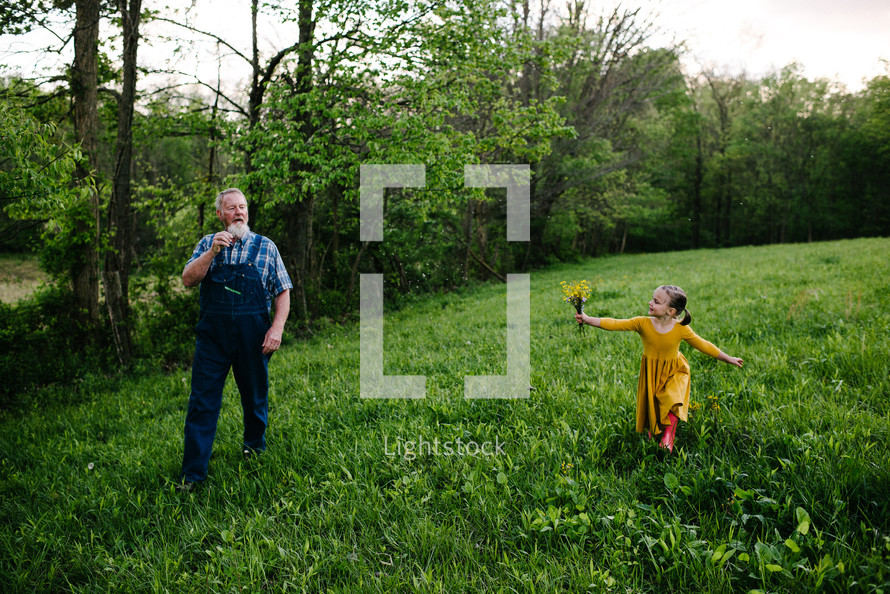 grandfather and granddaughter walking through a field of green grass