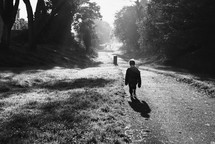 a toddler boy walking down a park trail under rays of sunlight 