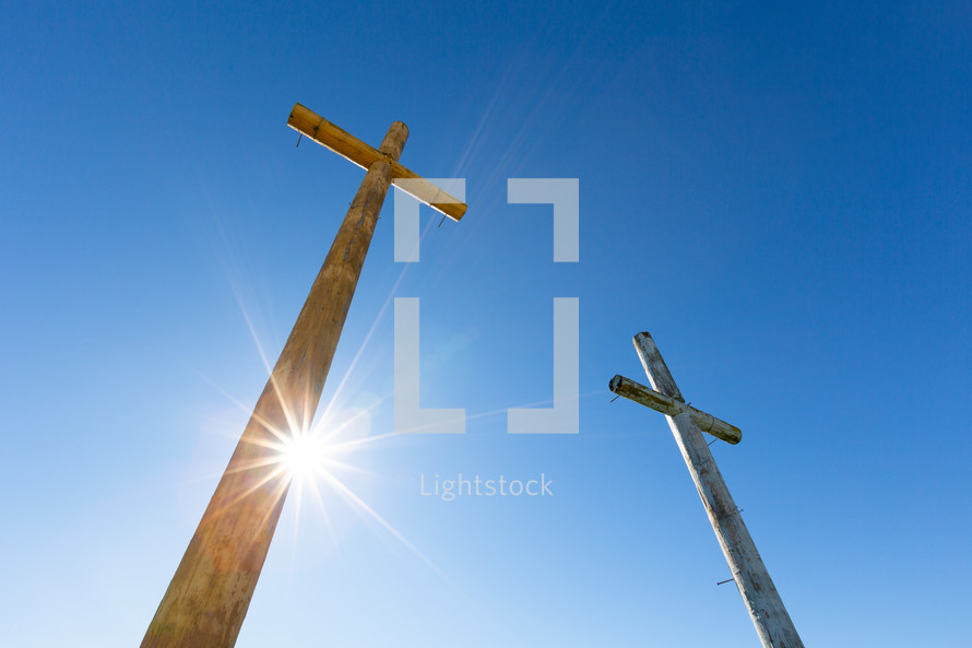 Sunlight on two wooden Christian crosses against blue sky