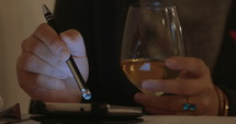 Close-up shot of a woman drinking white wine and scrolling on a smart phone with a stylus.