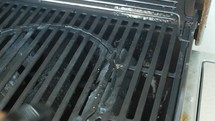 Man cleaning a greasy barbecue grill with a detergent spray bottle, ensuring a hygienic and spotless cooking surface