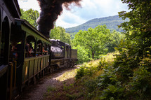 Smoky locomotive with passengers on scenic railway through forest and mountains