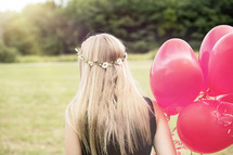 a girl with flowers in her hair walking with red balloons 