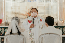 priest wearing a face mask speaking to a couple during a wedding 