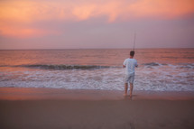 man standing on a beach with a fishing pole 