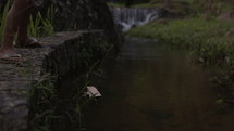 Boy picking paper boat out of stream - playing in summer - close up on hands