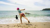 Girl throws ball for dog on a bright sunny beach on summer vacation