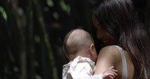Mother holding baby girl as she walks through park forest on summer day