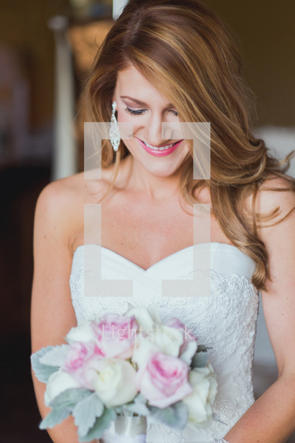 a smiling bride looking down at her bouquet 