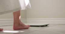 Pregnant woman steps onto bathroom scale - from behind close up on feet