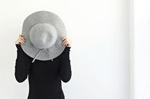 a woman hiding behind a hat 