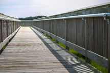 Wooden boardwalk with metal railings over coastal marsh
